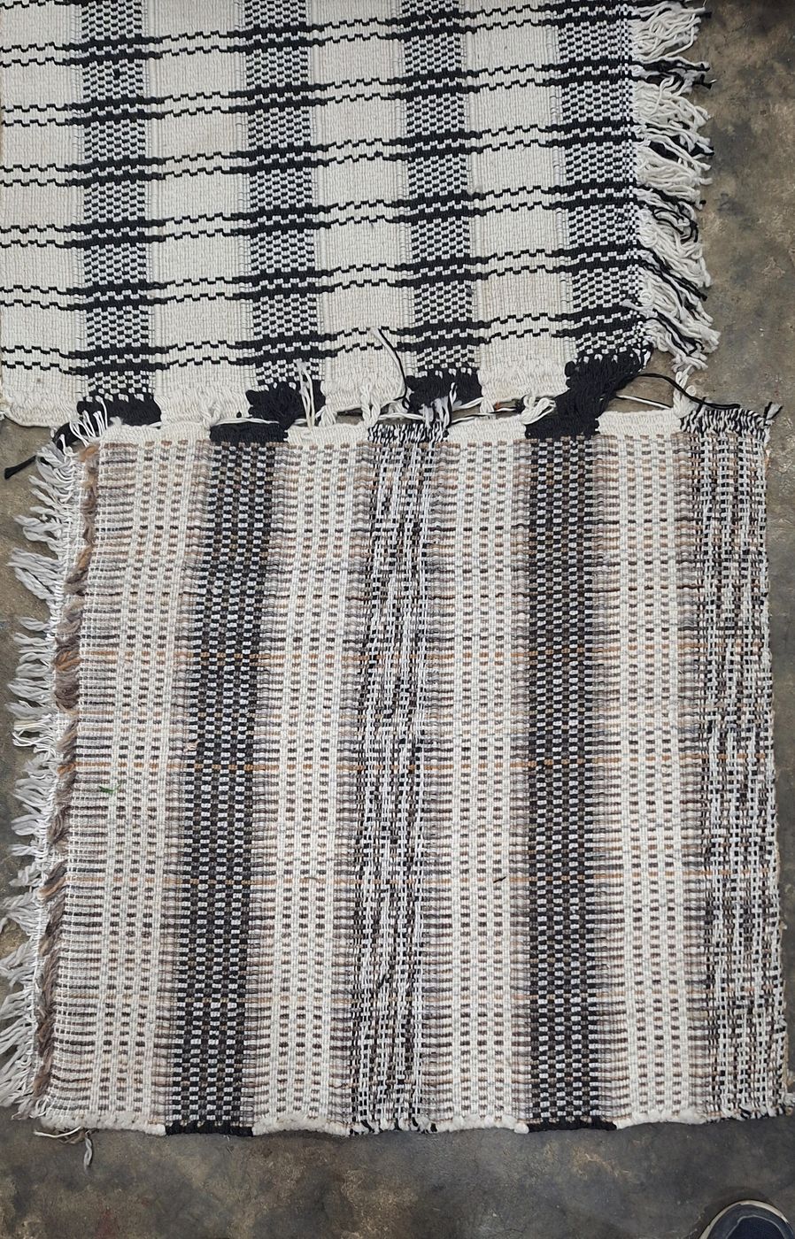 Two flatweave dhurries in black, cream and natural check, lying on a workshop floor