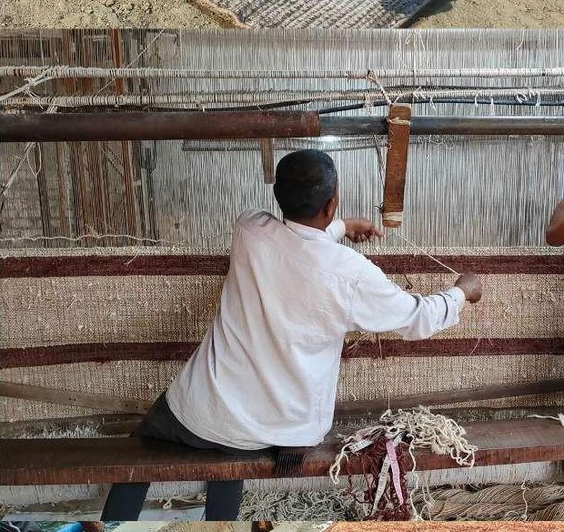 A weaver working across the warp threads of an upright loom